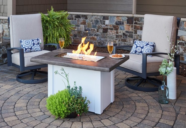 Patio furniture on a brick landing infront of a fire table in summer